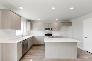 Kitchen with light brown cabinetry, light wood finished floors, recessed lighting, appliances with stainless steel finishes, and a kitchen island