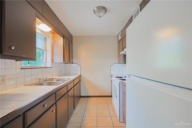 Kitchen featuring light tile patterned flooring, white appliances, tile countertops, a sink, and backsplash