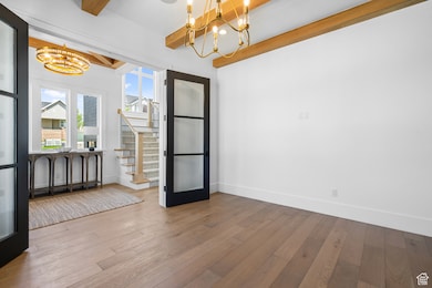 Unfurnished dining area featuring a chandelier, beamed ceiling, hardwood / wood-style flooring, and stairway