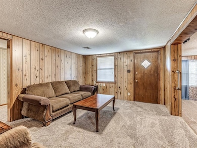 Carpeted living area featuring wooden walls and a textured ceiling