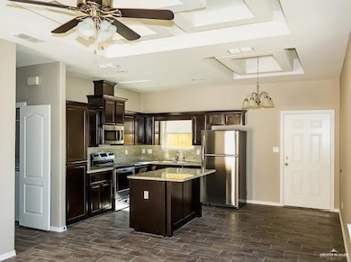 Kitchen featuring stainless steel appliances, dark wood-type flooring, a center island, decorative backsplash, and ceiling fan with notable chandelier