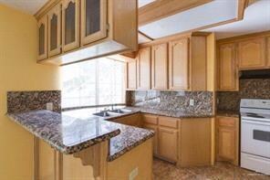 Kitchen with under cabinet range hood, backsplash, white electric range oven, a peninsula, and glass insert cabinets