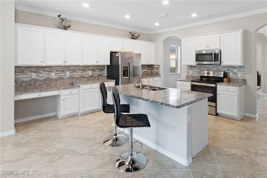 Kitchen featuring ornamental molding, arched walkways, stainless steel appliances, decorative backsplash, and recessed lighting
