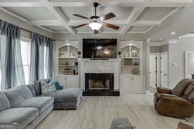 Living room with ceiling fan, coffered ceiling, a fireplace, light wood-style floors, and crown molding