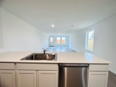 Spacious open-concept living area with ample natural light. The view includes a modern kitchen island with a sink and a dishwasher, leading to a large room with windows and a patio door.