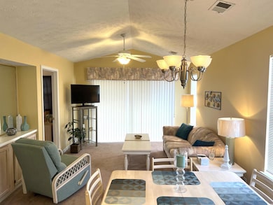 Carpeted living room featuring ceiling fan with notable chandelier, lofted ceiling, a textured ceiling, and plenty of natural light