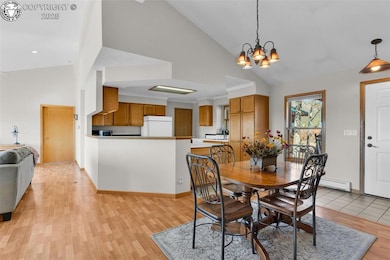 Dining area featuring high vaulted ceiling, light wood-type flooring, baseboard heating, and a chandelier