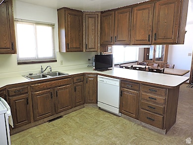Kitchen featuring a peninsula, light countertops, white appliances, and dark brown cabinetry