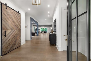 Corridor with a barn door, wood finished floors, ornamental molding, and recessed lighting