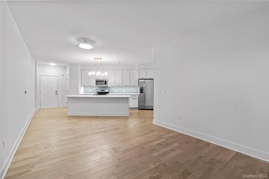 Kitchen with appliances with stainless steel finishes, white cabinetry, light wood-type flooring, light countertops, and a center island with sink
