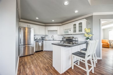 Kitchen with kitchen peninsula, sink, white cabinetry, dark wood-type flooring, and appliances with stainless steel finishes