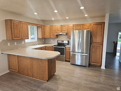 Kitchen with stainless steel appliances, light countertops, a peninsula,  oak cabinetry, and recessed lighting.