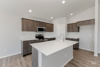 Kitchen featuring stainless steel appliances, modern cabinets, dark brown cabinetry, a kitchen island with sink, and light wood-style floors