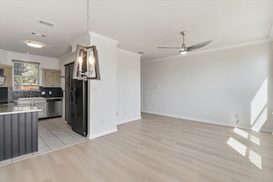 Kitchen featuring decorative backsplash, light stone countertops, black appliances, ornamental molding, and light wood-style floors