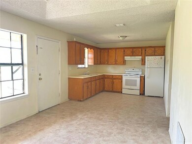 Kitchen with white appliances, under cabinet range hood, light flooring, light countertops, and brown cabinets
