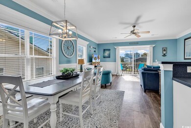 Dining room with healthy amount of natural light, ornamental molding, wood finished floors, wainscoting, and a chandelier
