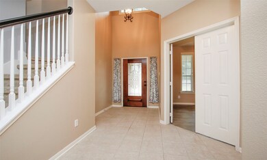 Two story entry with tile flooring, crown molding and plenty of room for a large entry table or bench. Staircase with white balusters, a wooden front door with leaded glass and side-lights.