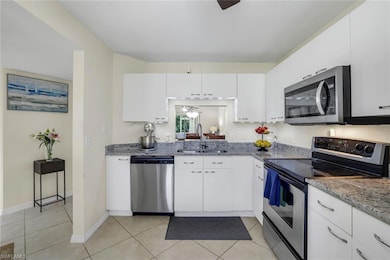 Kitchen with stainless steel appliances, light stone counters, white cabinetry, and ceiling fan
