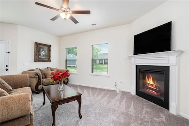 Living room featuring carpet floors, a glass covered fireplace, ceiling fan, and baseboards