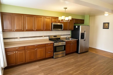 Kitchen with appliances with stainless steel finishes, a chandelier, brown cabinets, hanging light fixtures, and light wood-type flooring