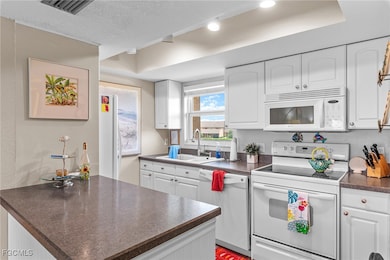 Kitchen featuring white appliances, dark countertops, white cabinetry, a peninsula, and a textured ceiling