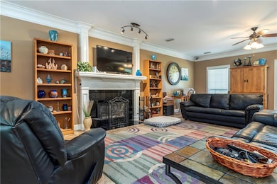Living area with crown molding, ceiling fan, a tiled fireplace, and ornate columns