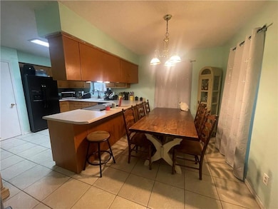 Kitchen with black fridge, a peninsula, light countertops, light tile patterned floors, and hanging light fixtures