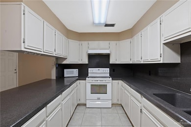 Kitchen with white appliances, white cabinetry, light tile patterned floors, under cabinet range hood, and visible vents