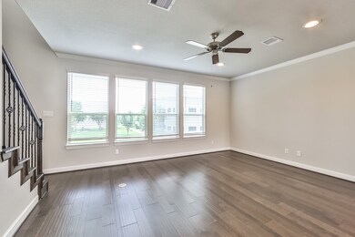 Bright living room with large windows, hardwood floors, and a ceiling fan. Features recessed lighting and a staircase with decorative railing. Perfect for a welcoming and airy atmosphere.