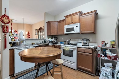 Kitchen featuring white appliances, light wood finished floors, a sink, brown cabinetry, and light stone countertops