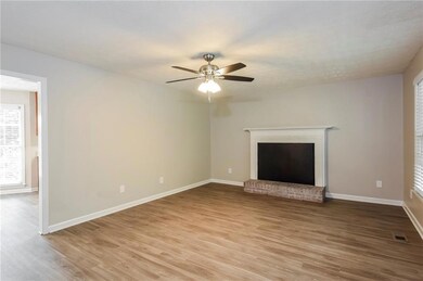 Unfurnished living room featuring light wood-style floors, a ceiling fan, baseboards, and a brick fireplace