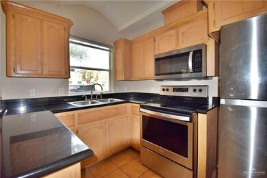 Kitchen with light tile patterned floors, lofted ceiling, dark countertops, stainless steel appliances, and a sink