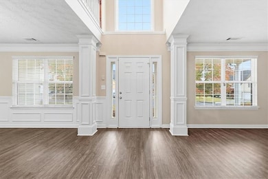 Foyer entrance featuring decorative columns, ornamental molding, dark wood-style flooring, a textured ceiling, and a towering ceiling