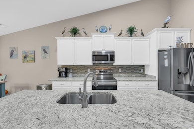 Kitchen featuring tasteful backsplash, stainless steel appliances, white cabinets, and light stone counters