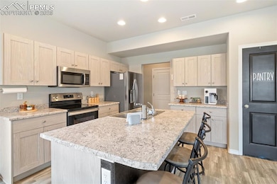 Kitchen with appliances with stainless steel finishes, a kitchen bar, light wood-style floors, light countertops, and a center island with sink