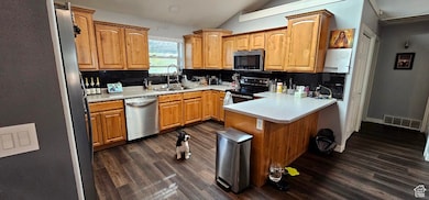 Kitchen with vaulted ceiling, decorative backsplash, stainless steel appliances, dark wood-style floors, and a peninsula