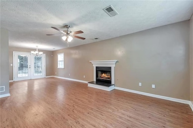 Unfurnished living room with baseboards, light wood finished floors, a glass covered fireplace, and a textured ceiling