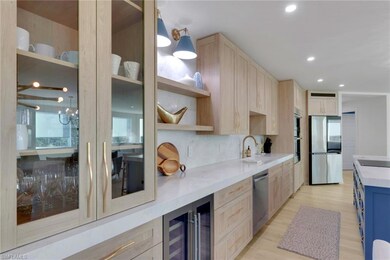Kitchen with light brown cabinetry, light stone counters, beverage cooler, appliances with stainless steel finishes, and recessed lighting