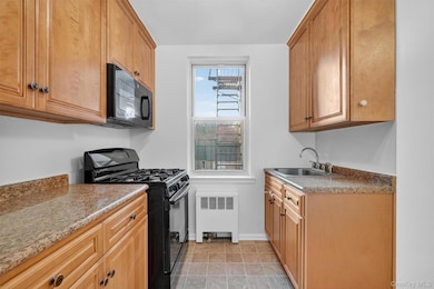 Kitchen with black appliances, radiator heating unit, brown cabinets, light stone counters, and light tile patterned flooring