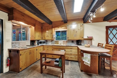 Kitchen with light countertops, decorative backsplash, stainless steel microwave, and a wood ceiling with exposed beams