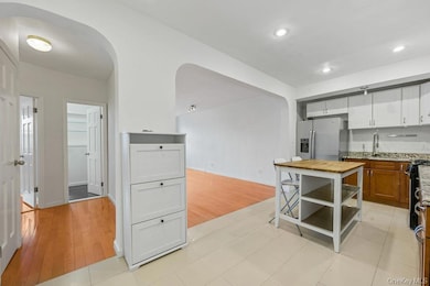 Kitchen featuring stainless steel refrigerator with ice dispenser, arched walkways, light stone countertops, black gas range, and white cabinetry