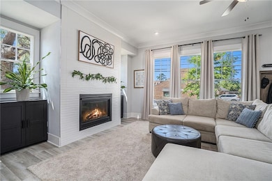 Living area featuring ornamental molding, a fireplace with flush hearth, a ceiling fan, light wood finished floors, and baseboards