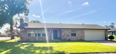 Single story home featuring brick siding, a garage, a chimney, and a front lawn