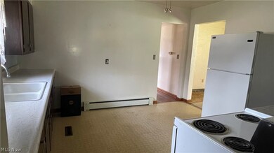 Kitchen featuring light colored carpet, a baseboard radiator, stove, sink, and white refrigerator
