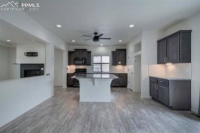 Kitchen featuring black microwave, gas range oven, a ceiling fan, light stone countertops, and a kitchen island