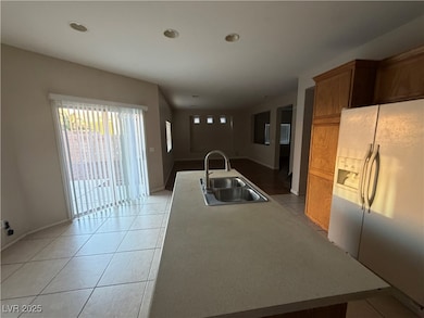 Kitchen featuring white fridge with ice dispenser, light tile patterned flooring, light countertops, a center island with sink, and recessed lighting