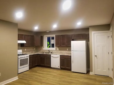 Kitchen featuring dark brown cabinetry, white appliances, light wood-style flooring, light countertops, and recessed lighting