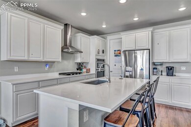 Kitchen with wood finished floors, recessed lighting, wall chimney range hood, appliances with stainless steel finishes, and a breakfast bar area