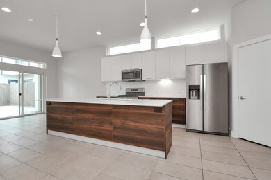 Stainless steel appliances, white cabinetry, and a contrasting wood-finish island. It features ample natural light and a minimalist design.