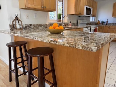 Kitchen featuring a breakfast bar area, white appliances, light stone counters, and a peninsula